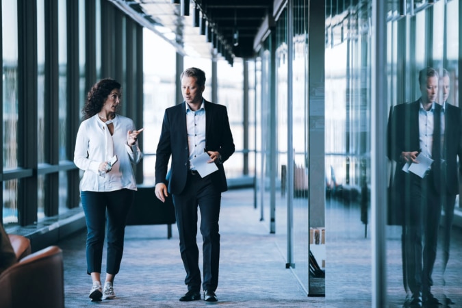 Two people walking down the hall of an office building in deep conversation
