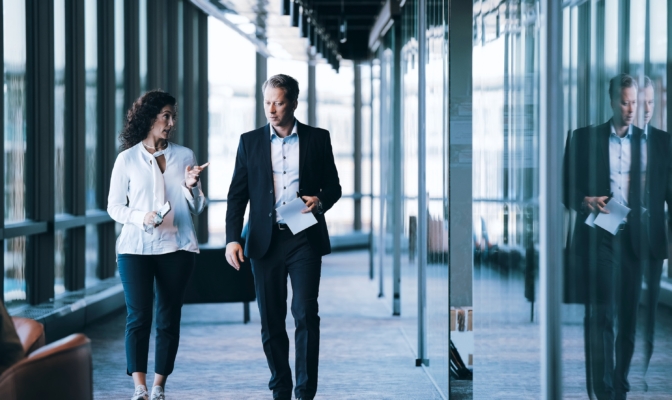 Confident Businesswoman Discussing With Male Entrepreneur While Walking In Corridor At Workplace